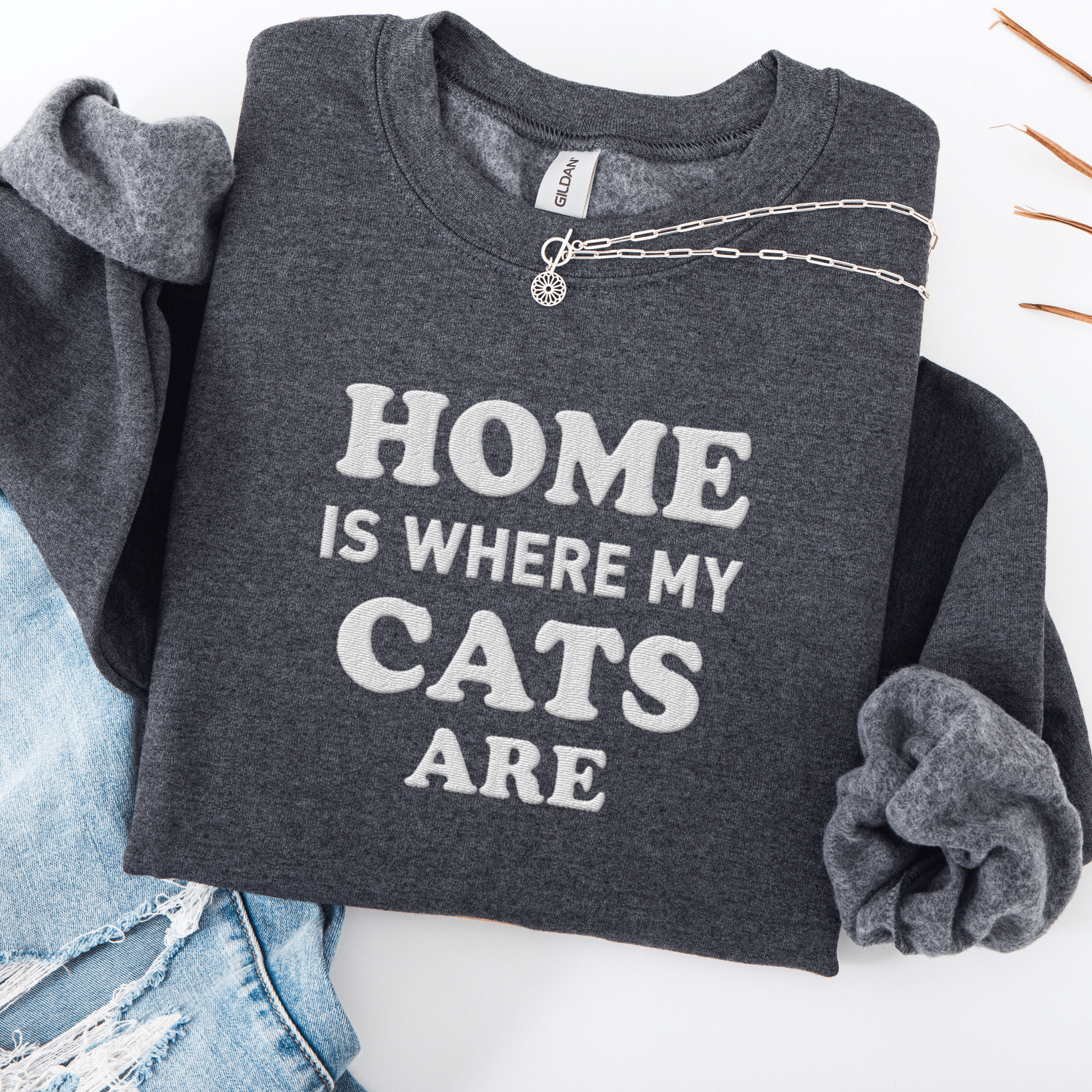 Dark Heather cat embroidered sweatshirt with “Home Is Where My Cats Are” text, folded flat on light denim