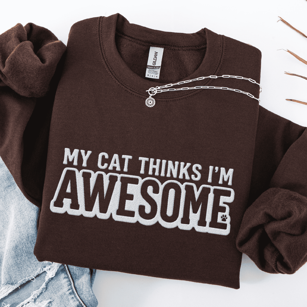 Dark Chocolate cat embroidered sweatshirt with “My Cat Thinks I’m Awesome” text, folded flat on light denim
