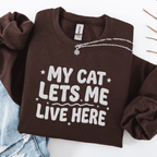 Dark Chocolate cat embroidered sweatshirt with “My Cat Lets Me Live Here” text, folded flat on light denim