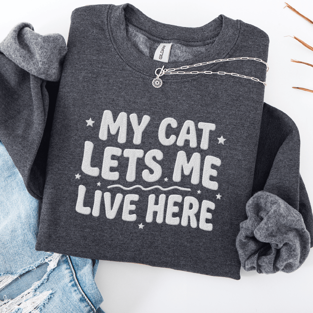 Dark Heather cat embroidered sweatshirt with “My Cat Lets Me Live Here” text, folded flat on light denim