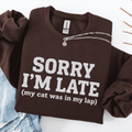 Dark Chocolate cat embroidered sweatshirt with “Sorry I’m Late (my cat was in my lap)” text, folded flat on light denim