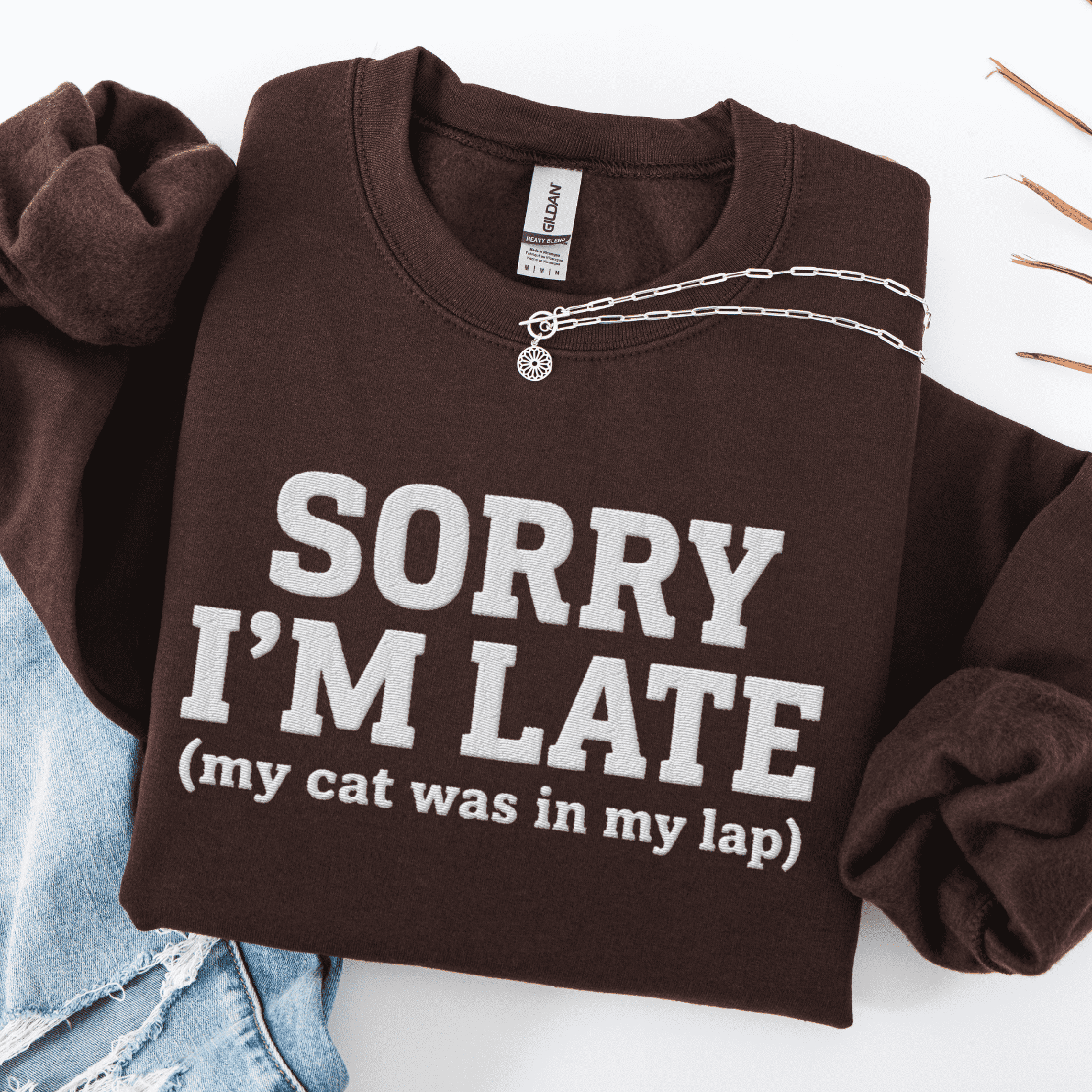 Dark Chocolate cat embroidered sweatshirt with “Sorry I’m Late (my cat was in my lap)” text, folded flat on light denim