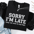 Black cat embroidered sweatshirt with “Sorry I’m Late” text, folded flat on light denim