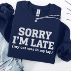 Navy cat embroidered sweatshirt with “Sorry I’m Late” text, folded flat on light denim