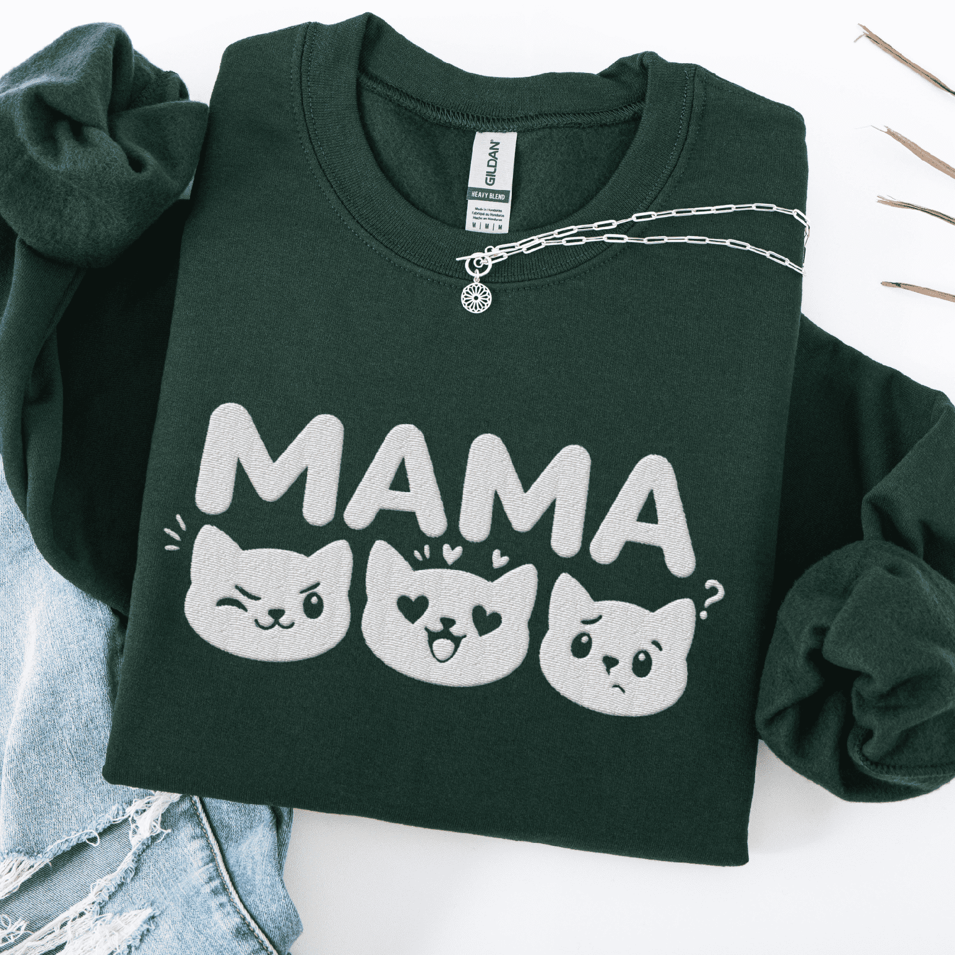 Forest Green mama embroidered sweatshirt with cat face design, folded flat on light denim