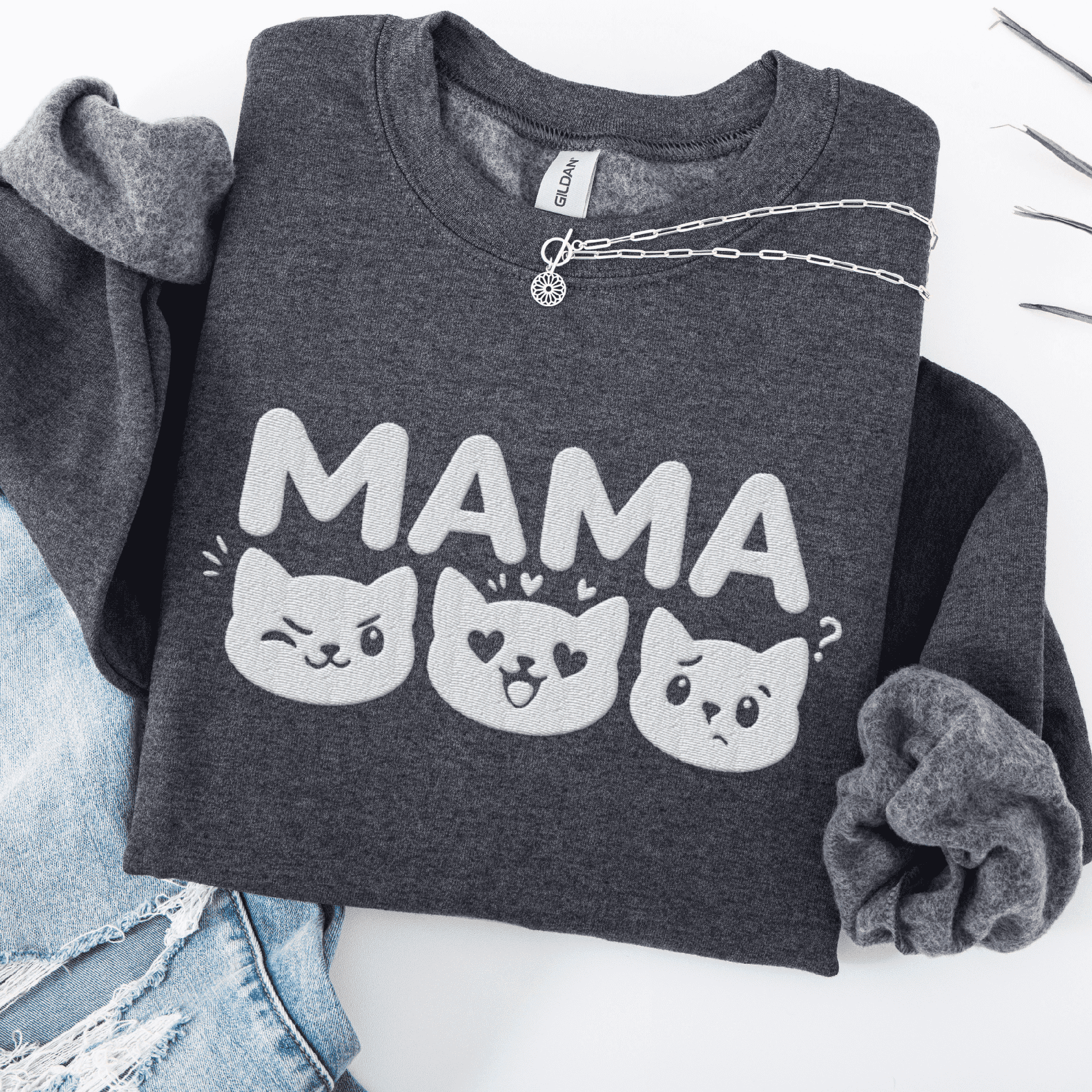 Dark Heather mama embroidered sweatshirt with cat face design, folded flat on light denim