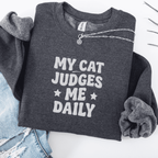 Dark Heather cat embroidered sweatshirt with “My Cat Judges Me Daily” text, folded flat on light denim