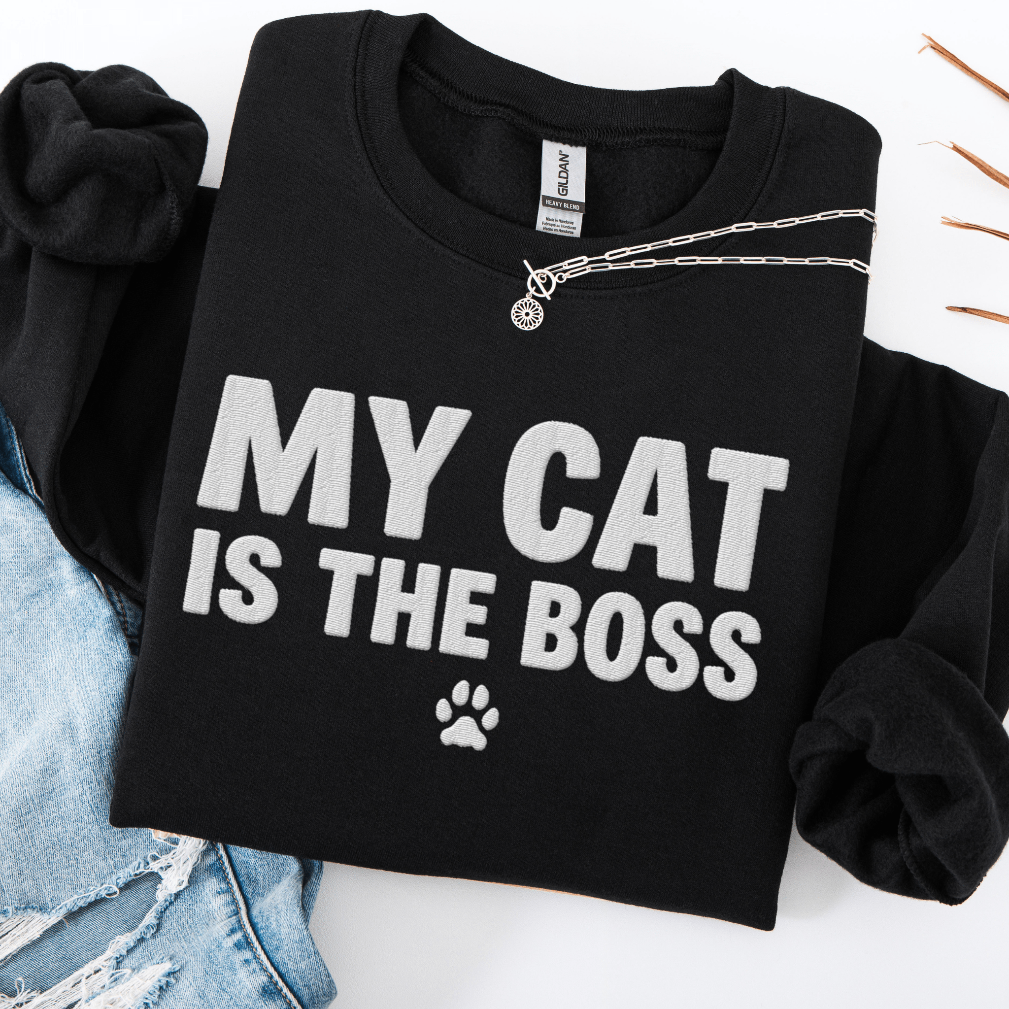 Black cat embroidered sweatshirt with “My Cat Is The Boss” text, folded flat on light denim