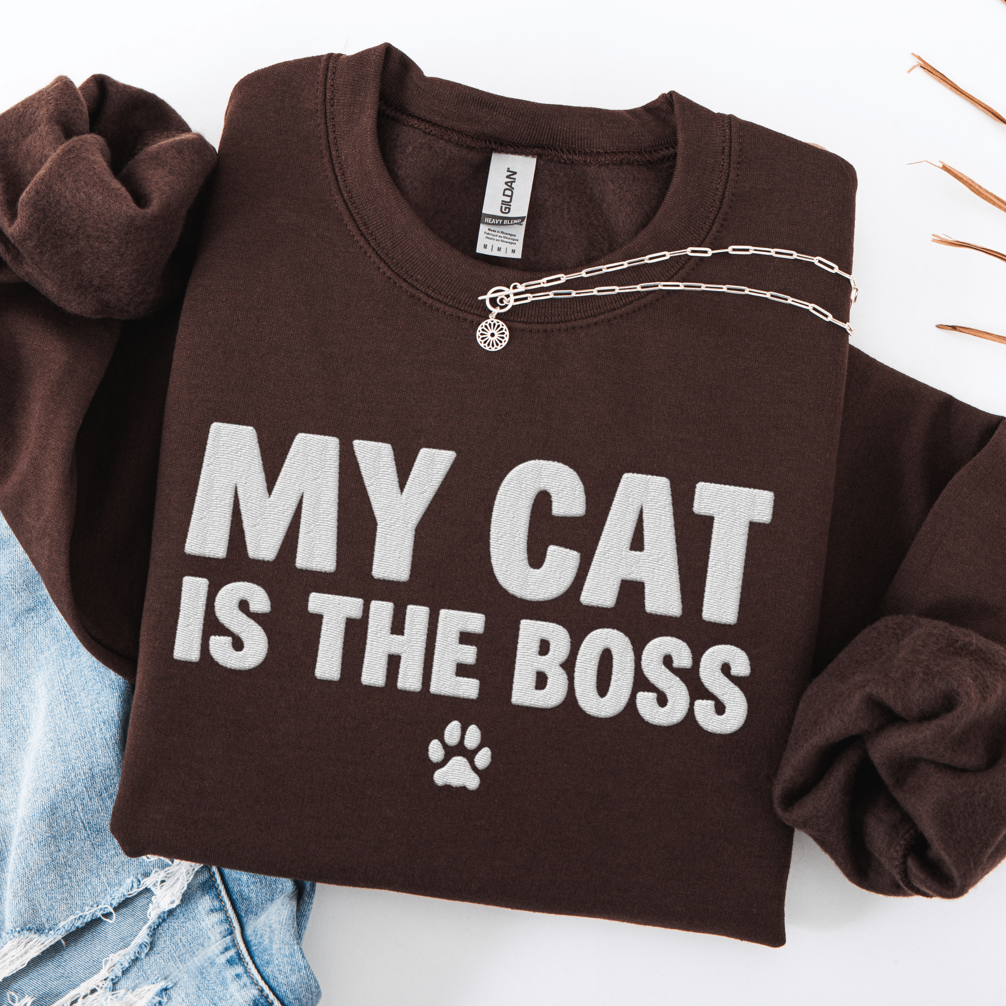 Dark Chocolate cat embroidered sweatshirt with “My Cat Is The Boss” text, folded flat on light denim