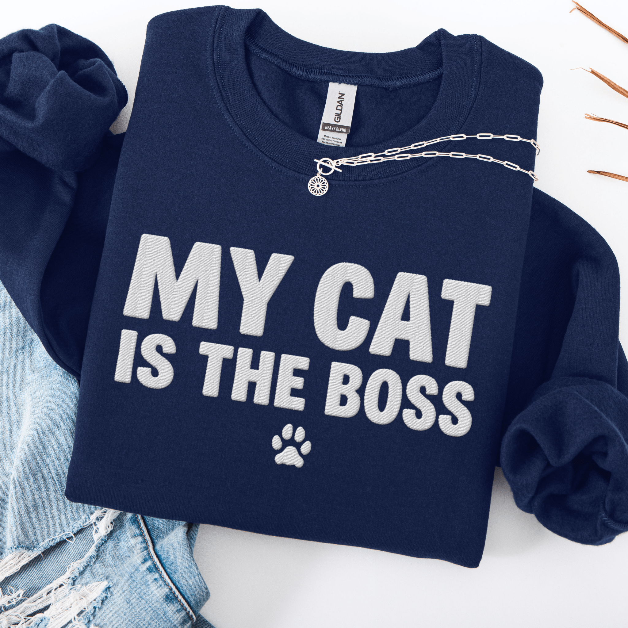 Navy cat embroidered sweatshirt with “My Cat Is The Boss” text, folded flat on light denim
