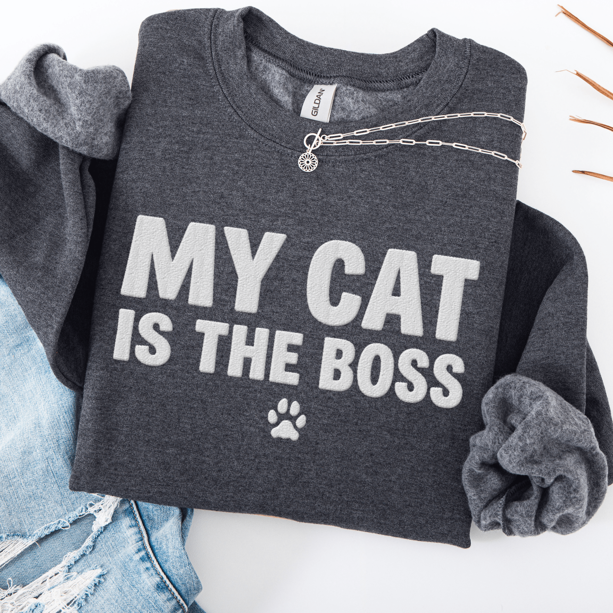 Dark Heather cat embroidered sweatshirt with “My Cat Is The Boss” text, folded flat on light denim