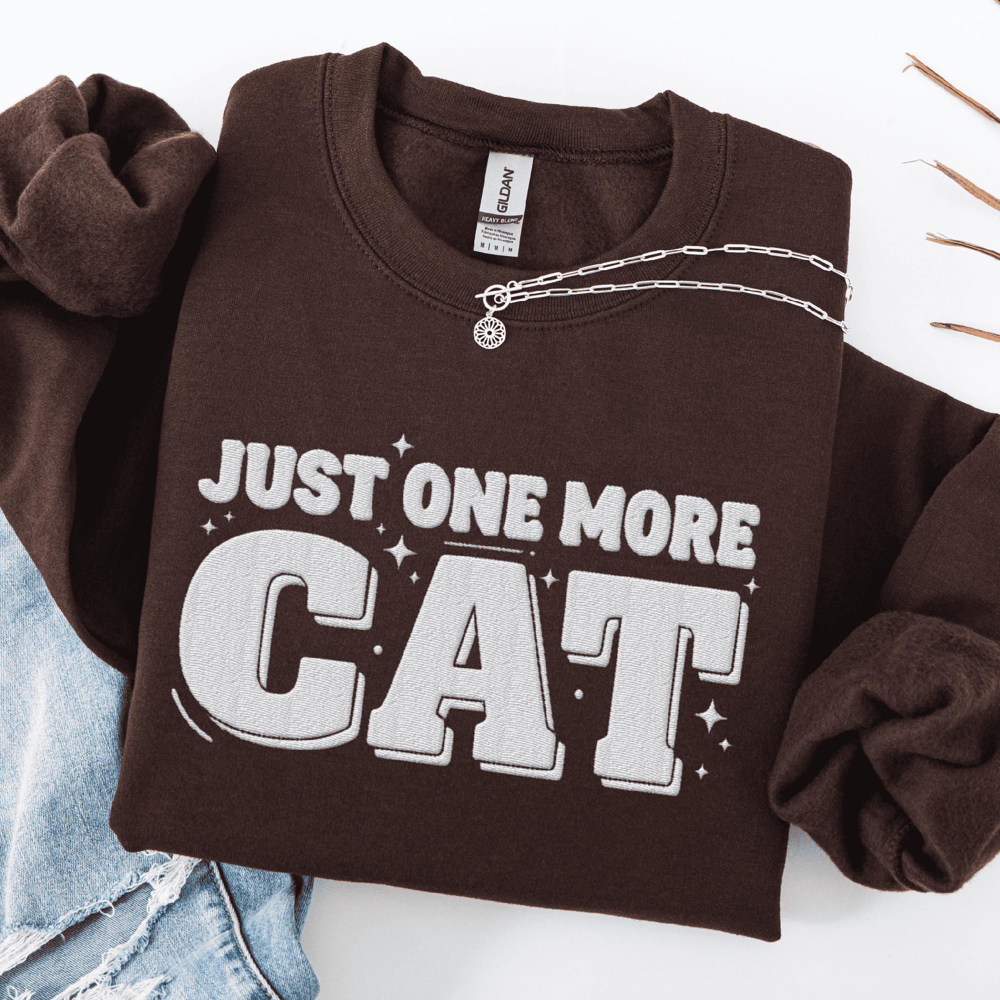 Dark Chocolate one more cat embroidered sweatshirt with “Just One More Cat” text, folded flat on light denim