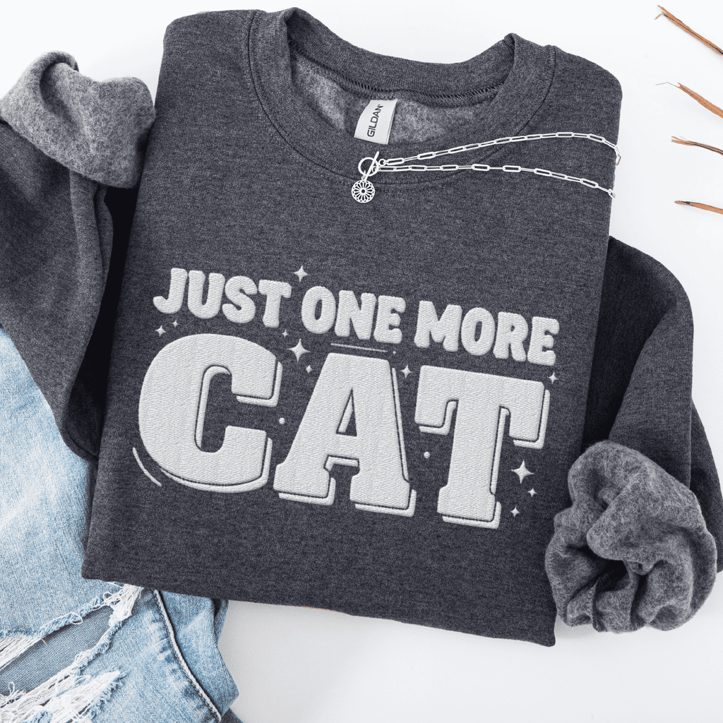 Dark Heather one more cat embroidered sweatshirt with “Just One More Cat” text, folded flat on light denim