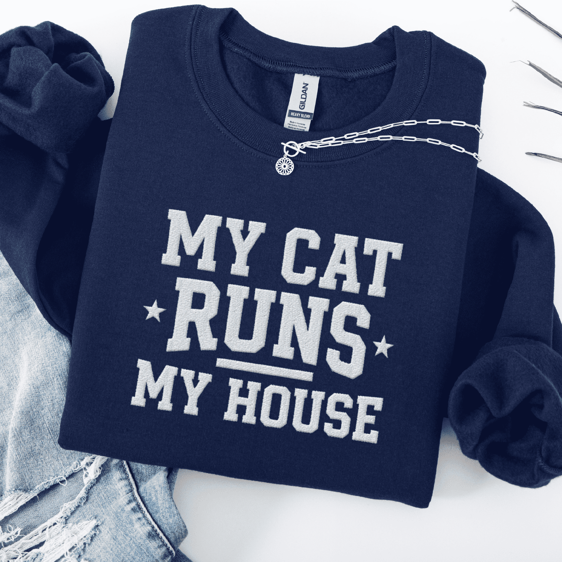Navy cat embroidered sweatshirt with “My Cat Runs My House” text, folded flat on light denim