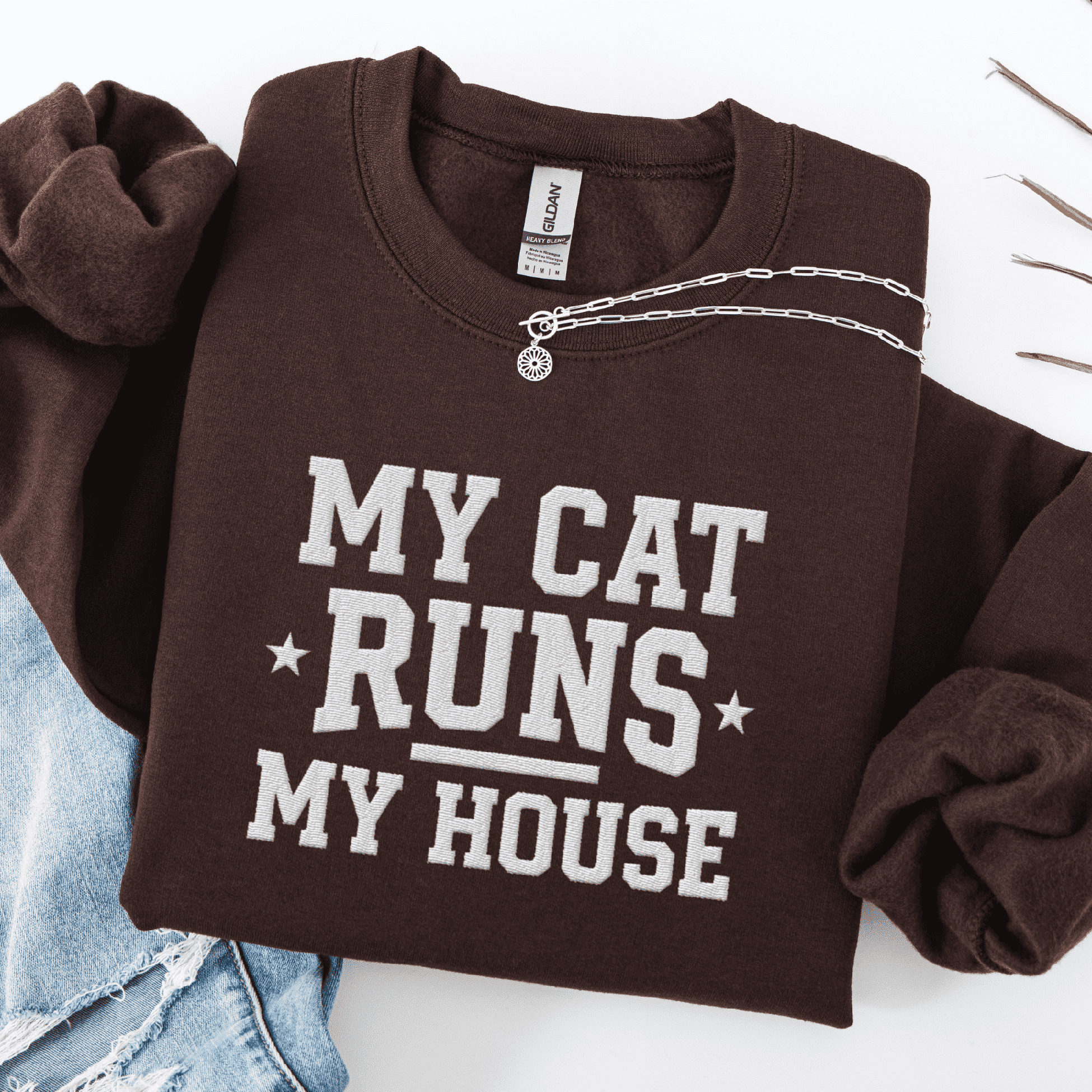 Dark Chocolate cat embroidered sweatshirt with “My Cat Runs My House” text, folded flat on light denim