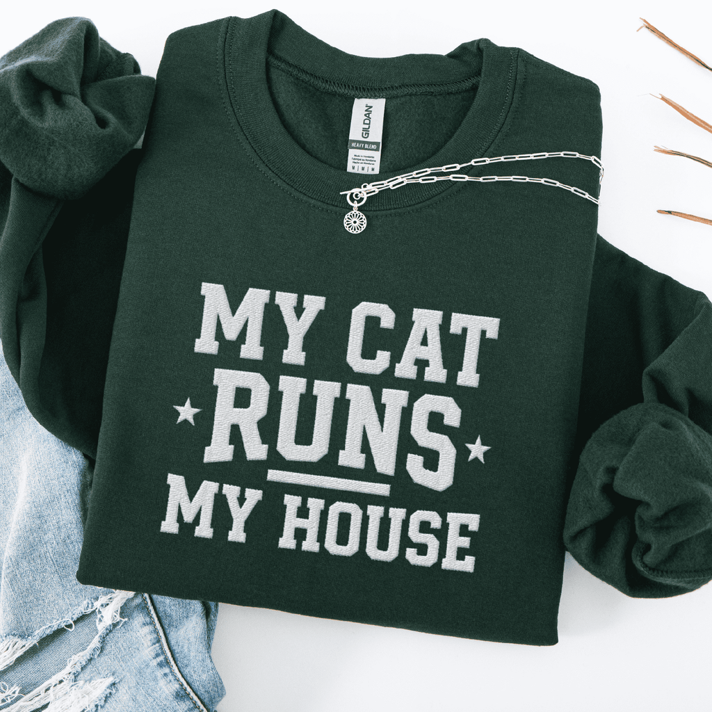 Forest Green cat embroidered sweatshirt with “My Cat Runs My House” text, folded flat on light denim