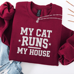 Maroon cat embroidered sweatshirt with “My Cat Runs My House” text, folded flat on light denim