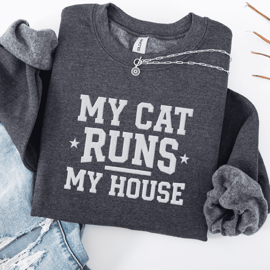 Dark Heather cat embroidered sweatshirt with “My Cat Runs My House” text, folded flat on light denim