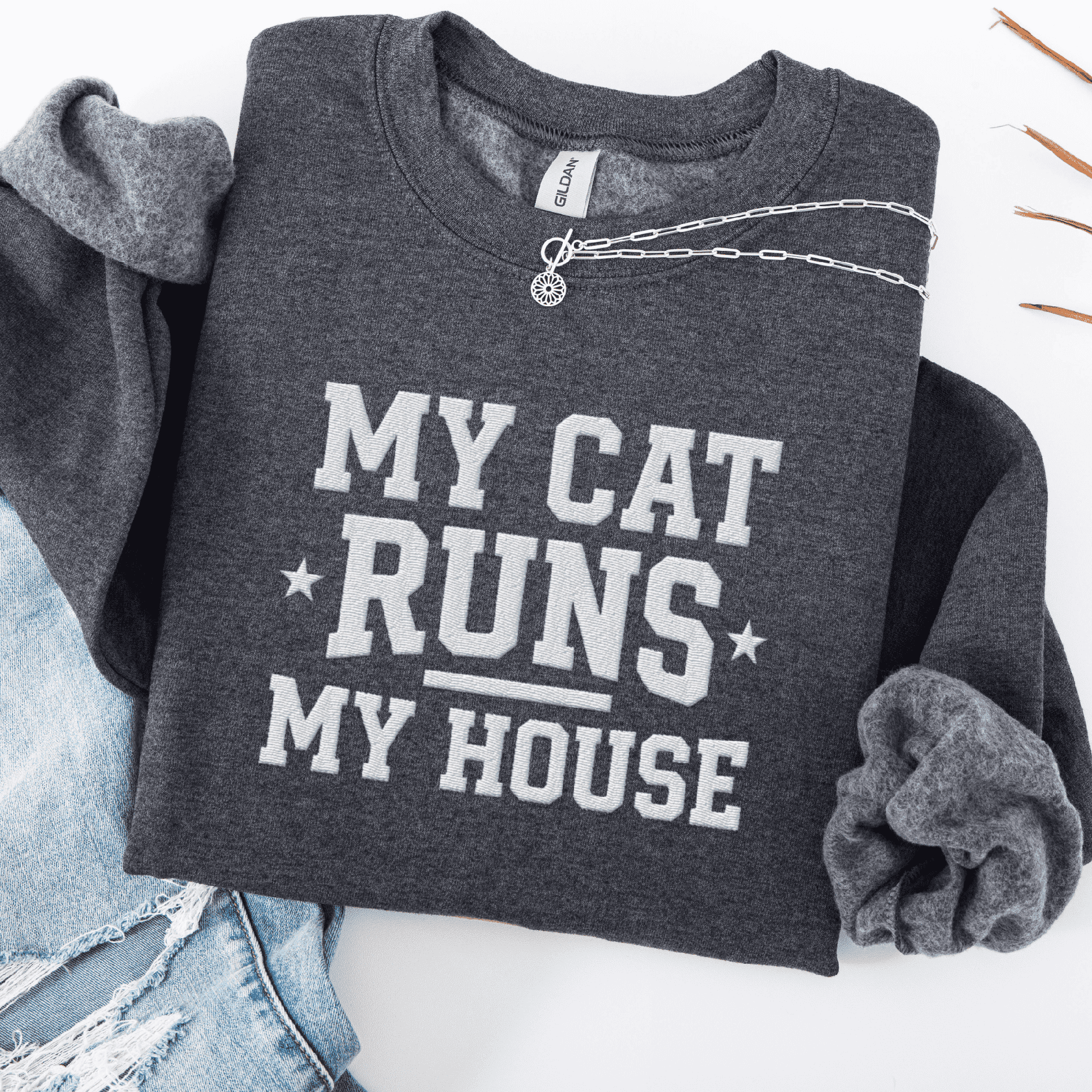 Dark Heather cat embroidered sweatshirt with “My Cat Runs My House” text, folded flat on light denim