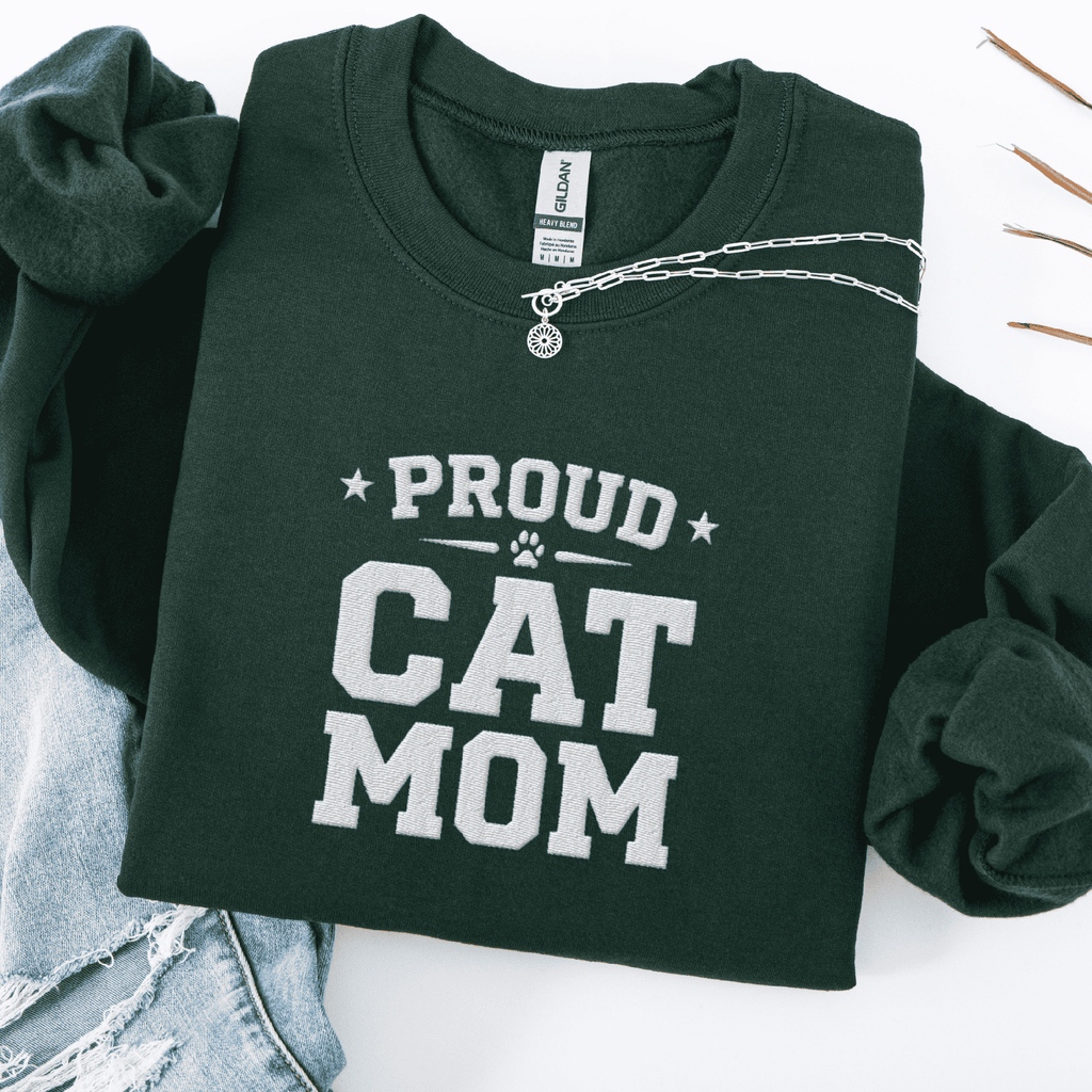 Forest Green proud cat mom embroidered sweatshirt with “Proud Cat Mom” text, folded flat on light denim