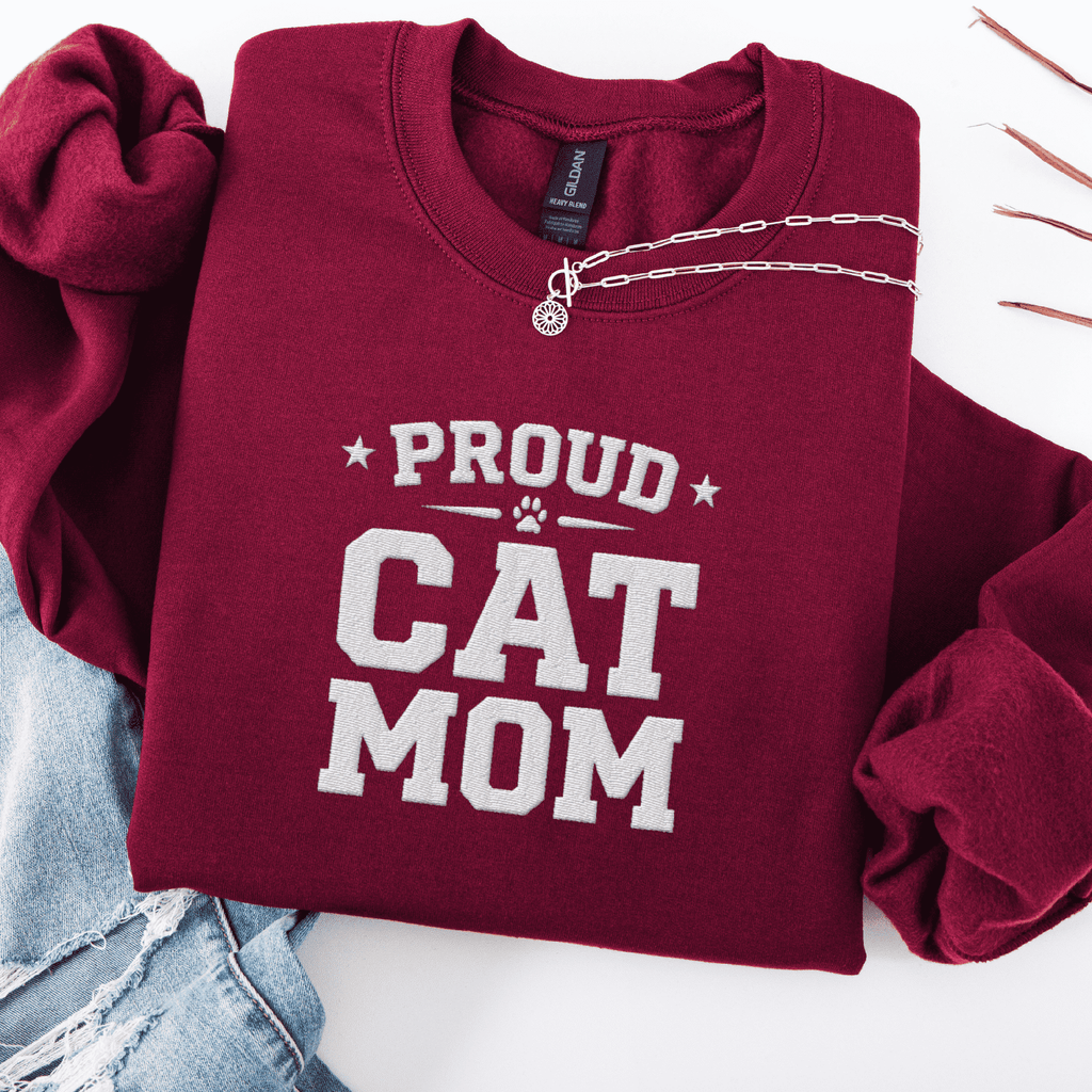 Maroon proud cat mom embroidered sweatshirt with “Proud Cat Mom” text, folded flat on light denim