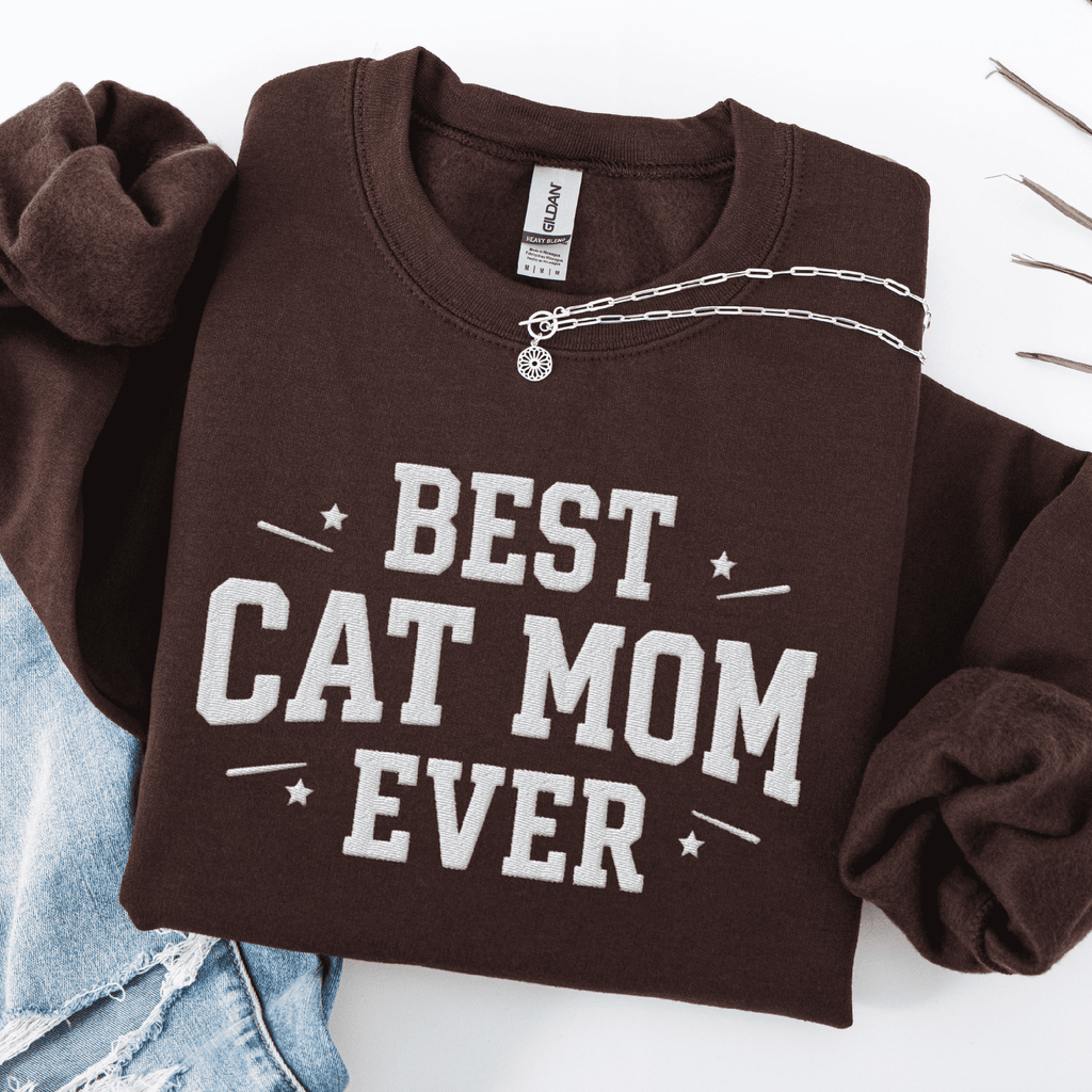 Dark Chocolate cat mom embroidered sweatshirt with “Best Cat Mom Ever” text, folded flat on light denim