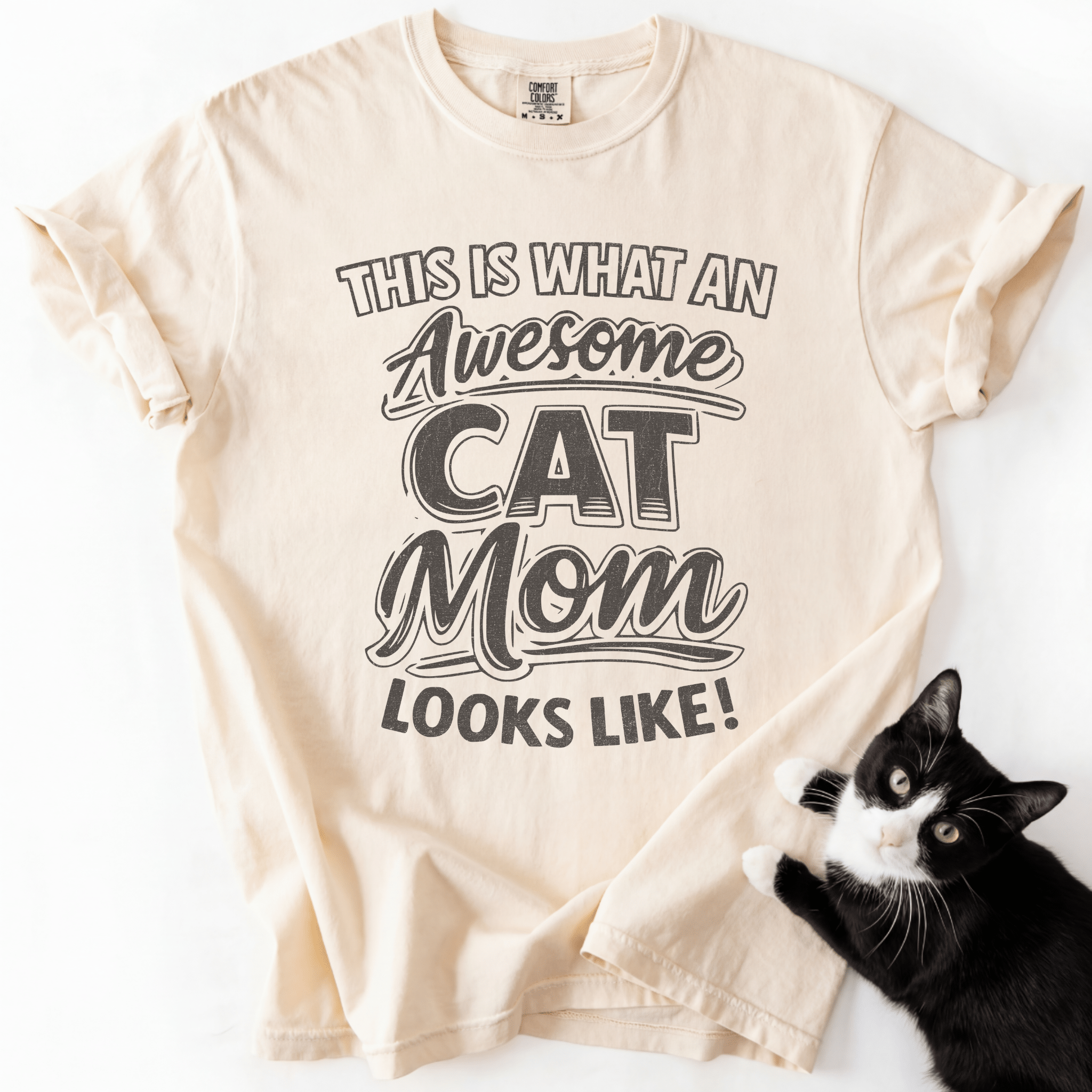 Ivory cat mom t-shirt with “This Is What an Awesome Cat Mom Looks Like” graphic displayed in a flat lay with a black cat