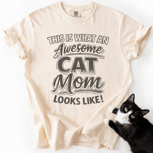 Ivory cat mom t-shirt with “This Is What an Awesome Cat Mom Looks Like” graphic displayed in a flat lay with a black cat