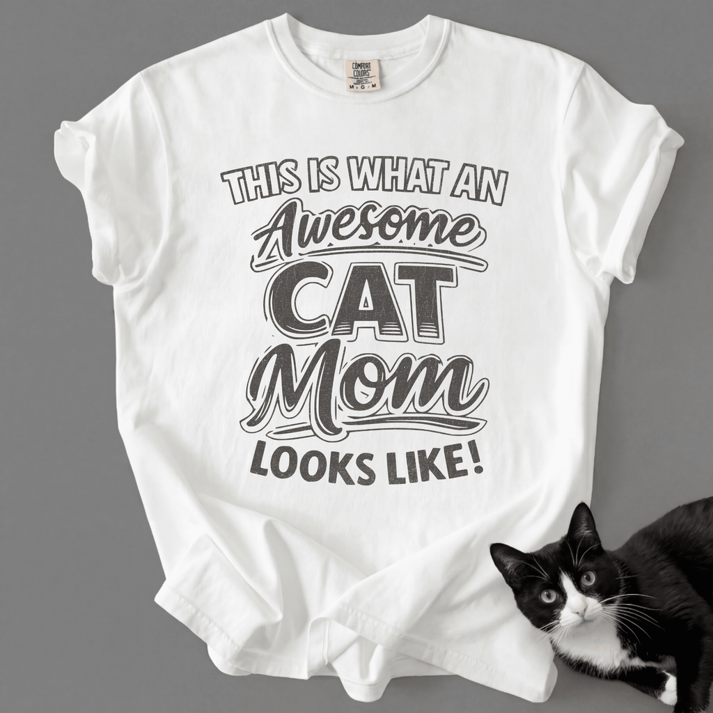 White cat mom t-shirt with “This Is What an Awesome Cat Mom Looks Like” graphic shown with a black cat at the bottom corner