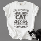 White cat mom t-shirt with “This Is What an Awesome Cat Mom Looks Like” graphic shown with a black cat at the bottom corner