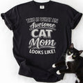 Black cat mom t shirt with “This Is What an Awesome Cat Mom Looks Like” design and black and white cat beside the shirt