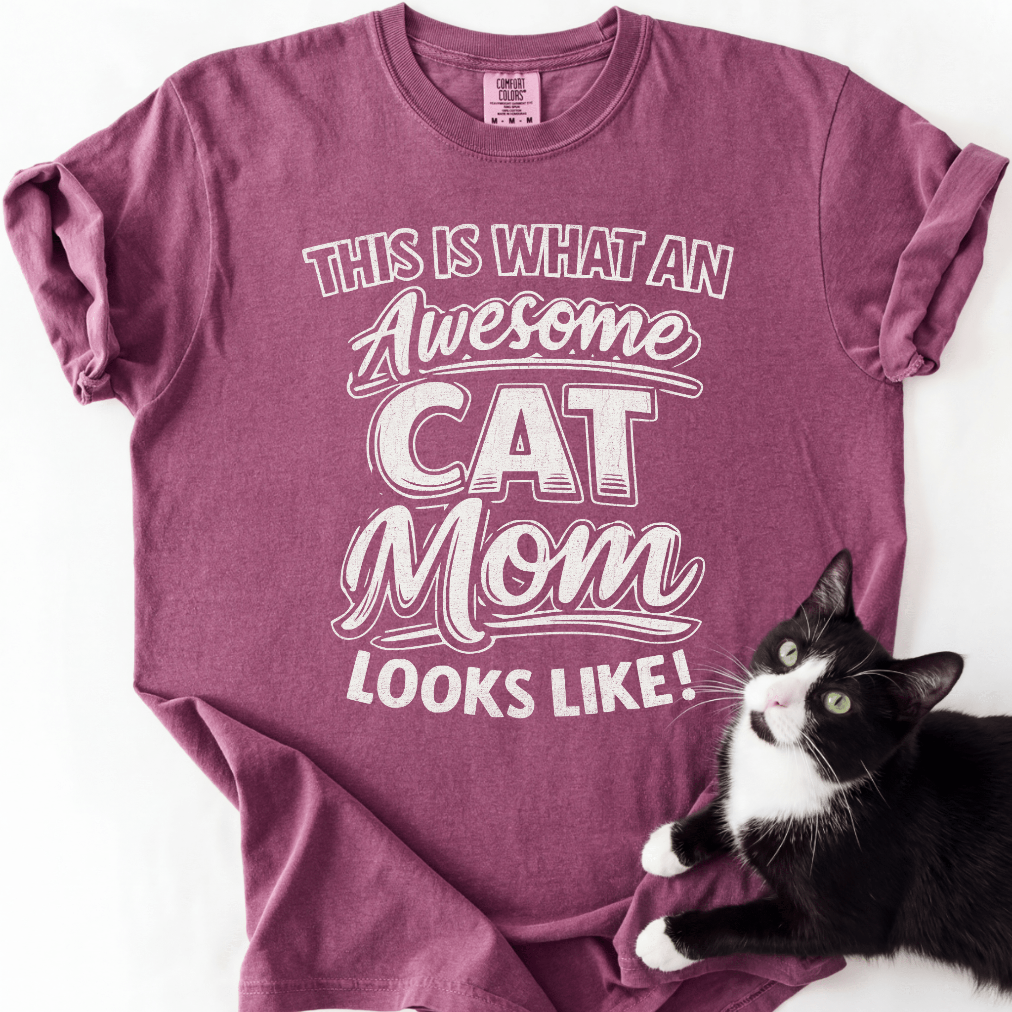 Berry cat mom t shirt with “This Is What an Awesome Cat Mom Looks Like” design and black and white cat beside the shirt
