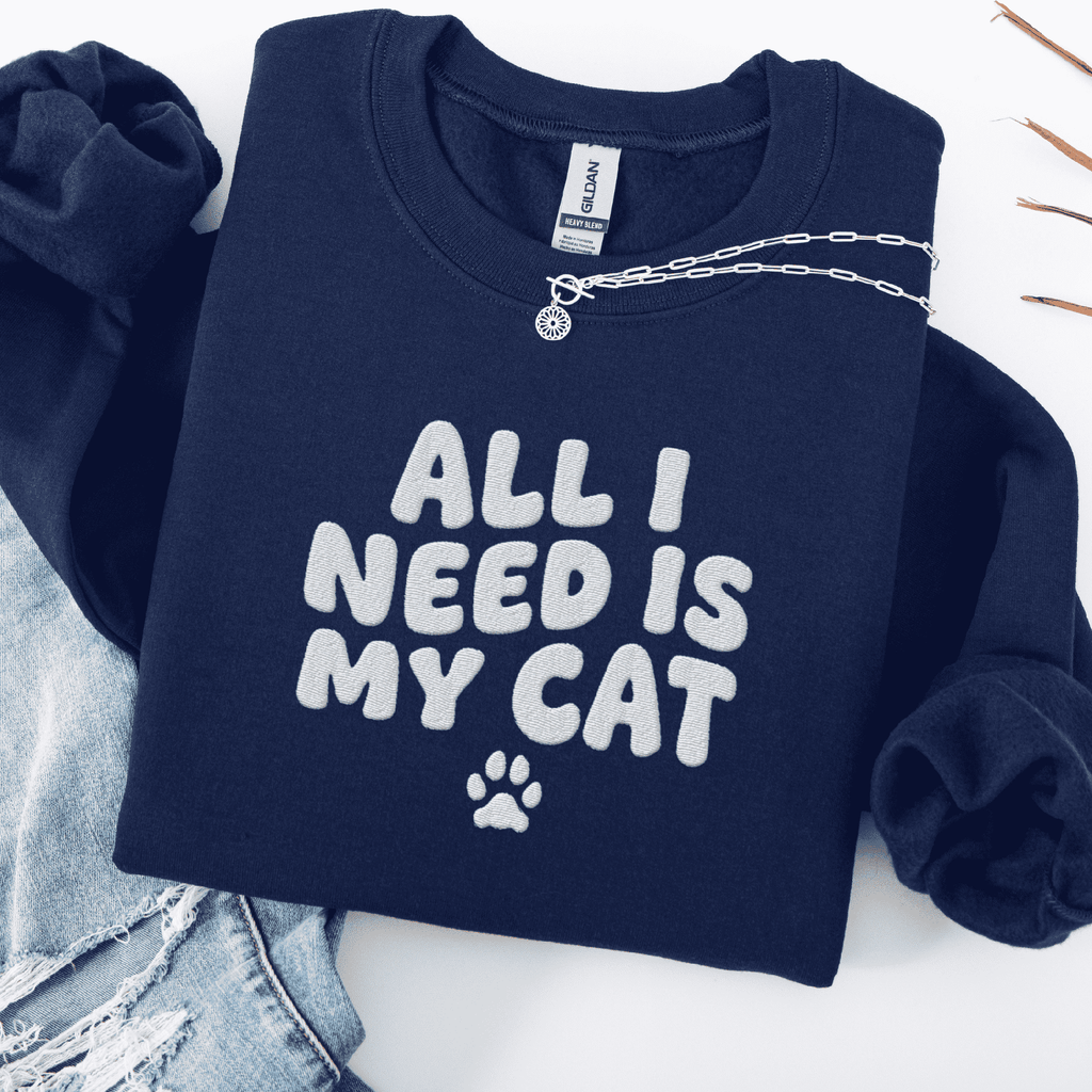 Navy embroidered cat sweatshirt with the phrase “All I Need Is My Cat” shown folded flat