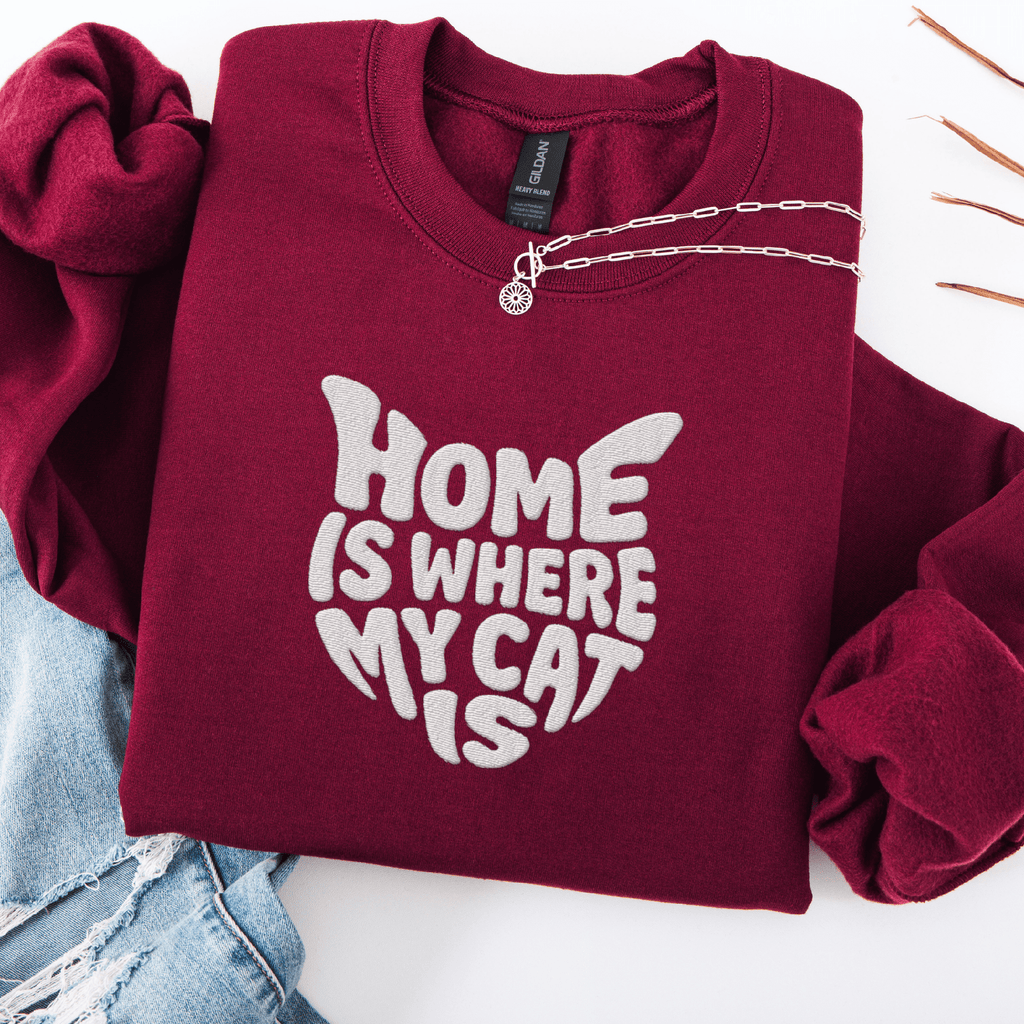 Maroon embroidered cat sweatshirt with the phrase “Home Is Where My Cat Is” shown folded flat
