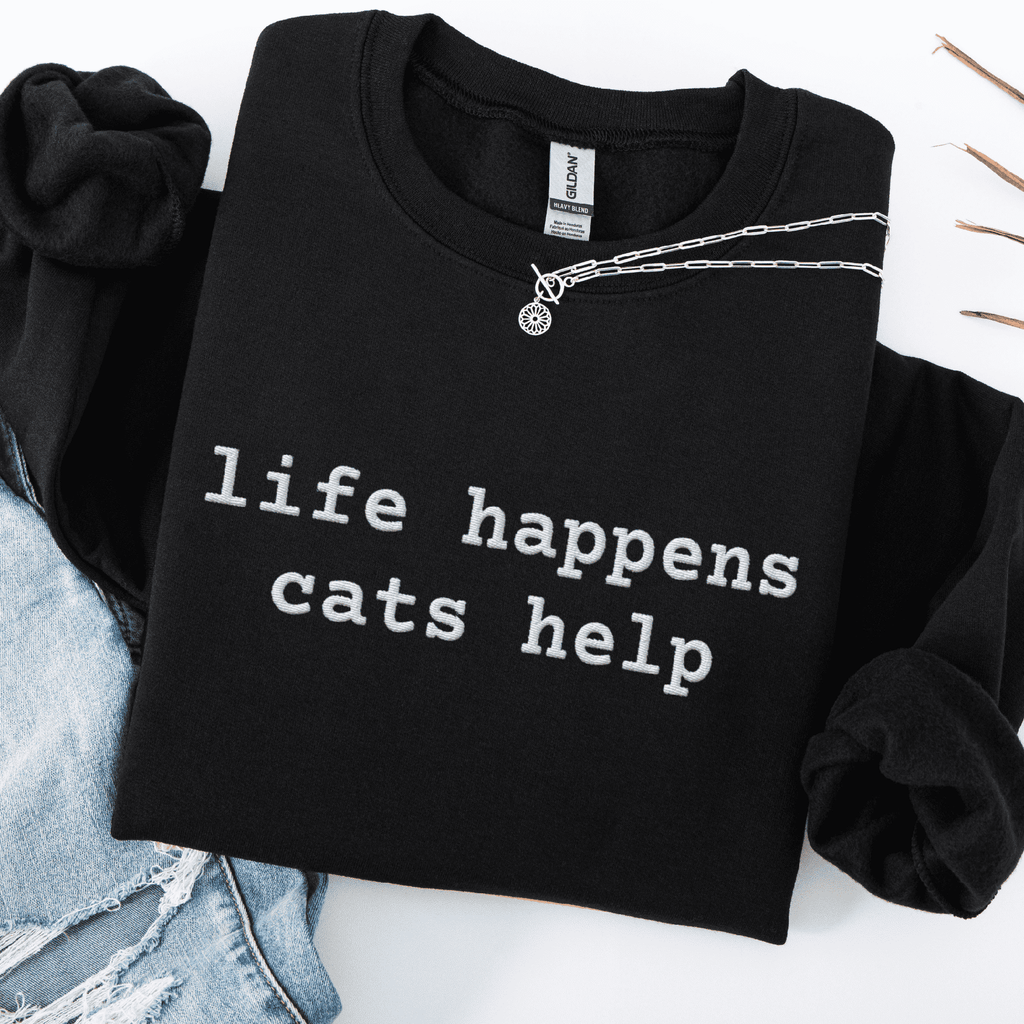 Black embroidered cat sweatshirt with the phrase “life happens cats help” shown folded flat