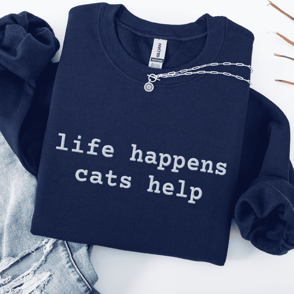 Navy embroidered cat sweatshirt with the phrase “life happens cats help” shown folded flat