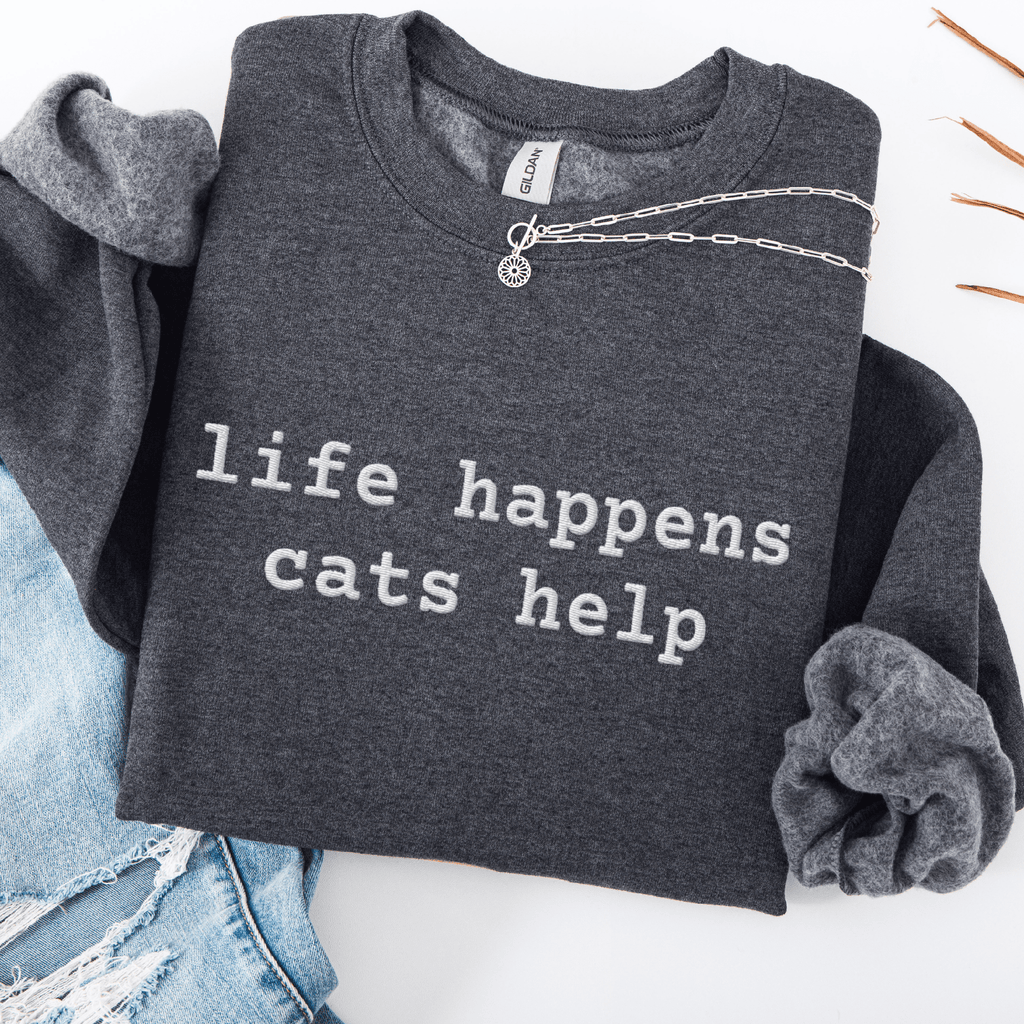 Dark Heather embroidered cat sweatshirt with the phrase “life happens cats help” shown folded flat