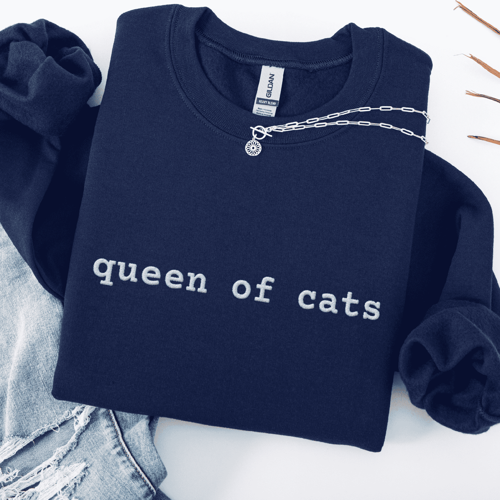 Navy embroidered cat sweatshirt with the phrase “queen of cats” shown folded flat