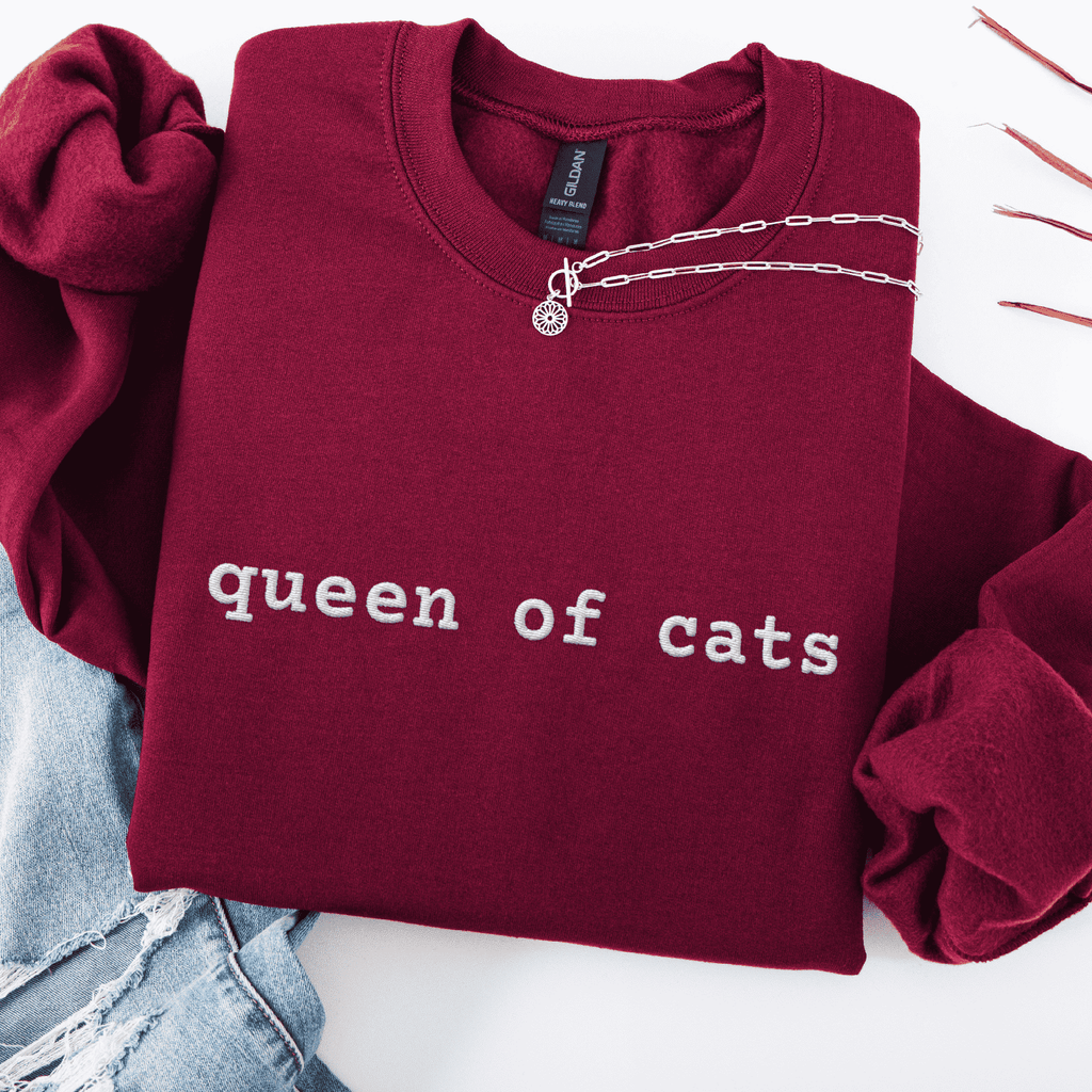 Maroon embroidered cat sweatshirt with the phrase “queen of cats” shown folded flat