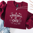 Maroon embroidered cat sweatshirt with “Queen of Cats” text and cat-themed doodle icons shown folded flat