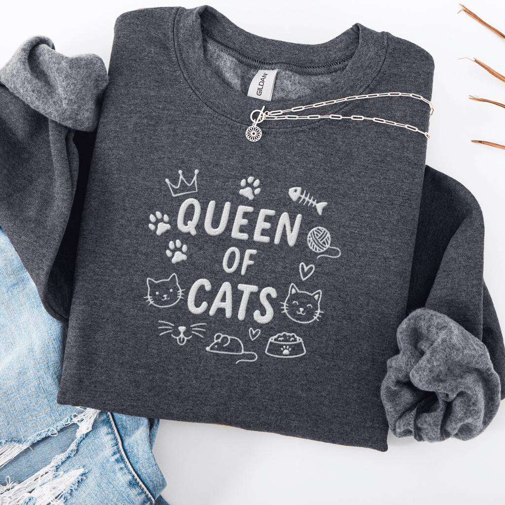 Dark Heather embroidered cat sweatshirt with “Queen of Cats” text and cat-themed doodle icons shown folded flat