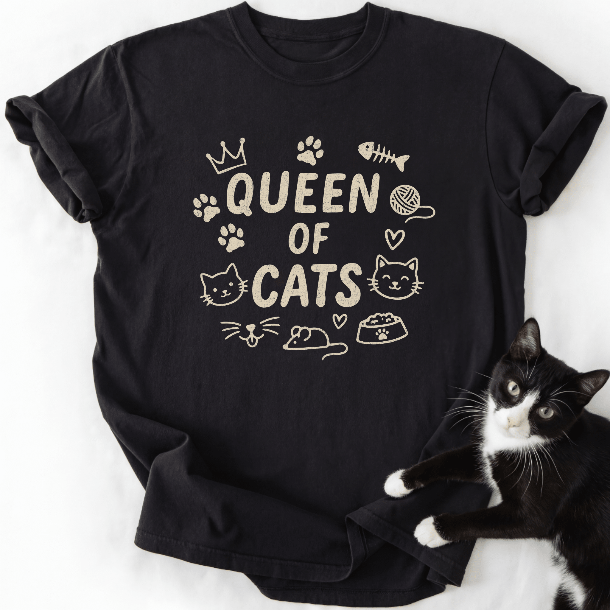 Black Queen of Cats cat t shirt with cat-themed doodle icons shown laid flat with a tuxedo cat beside it
