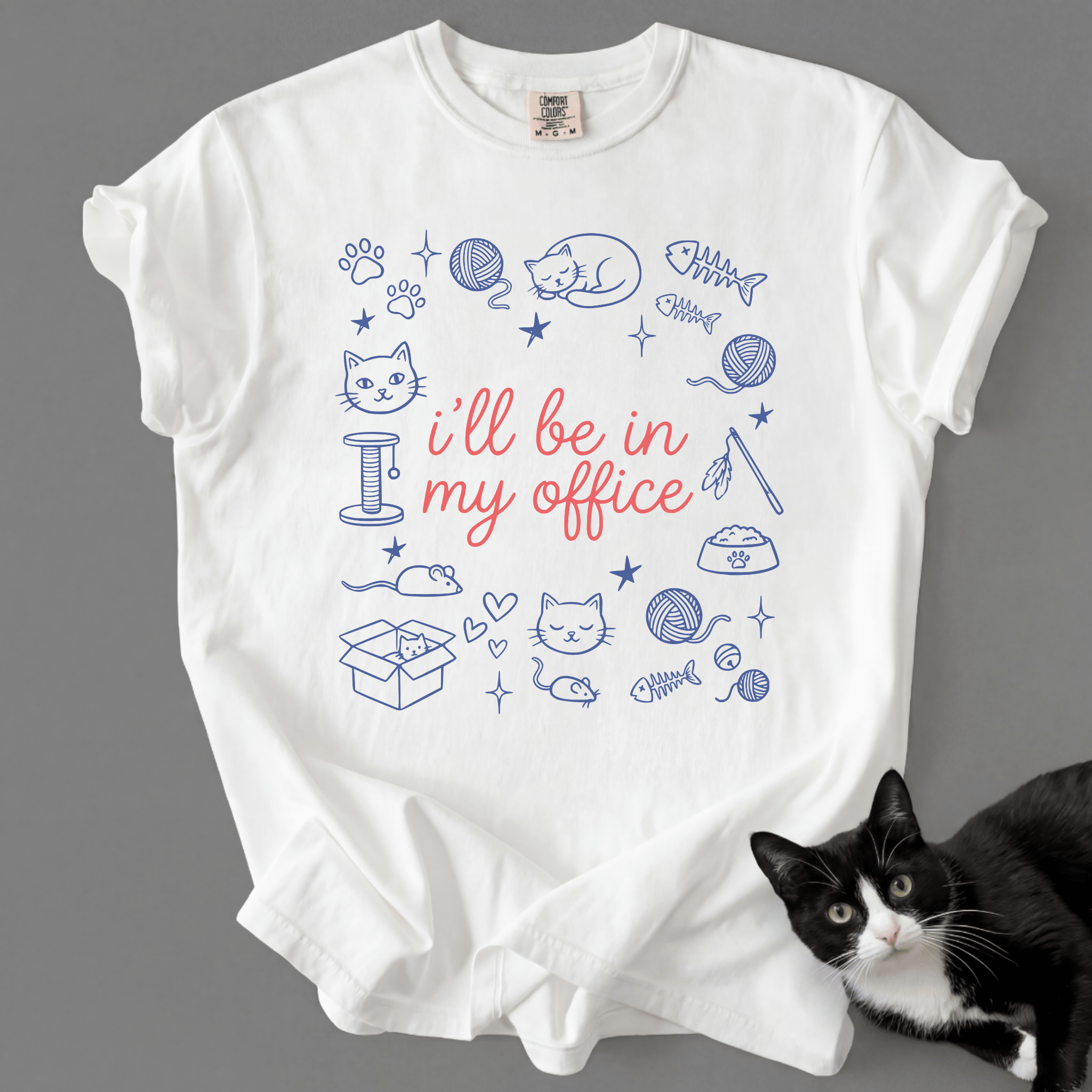 White funny cat t shirt with I'll be in my office text and pastel cat office illustration, shown flat with a black cat beside it