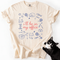 Ivory funny cat t shirt with I'll be in my office text and pastel cat themed office doodles, shown flat with a black cat beside it
