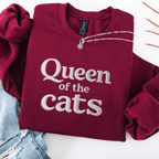 Maroon cat embroidered sweatshirt with Queen of the Cats text folded flat with jeans