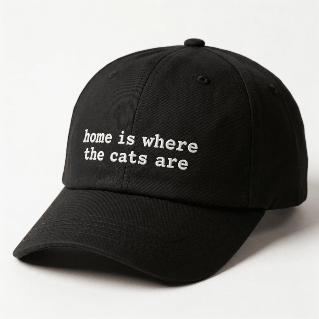Angled front view of a black embroidered cap with home is where the cats are text on the front