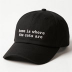 Angled front view of a black embroidered cap with home is where the cats are text on the front