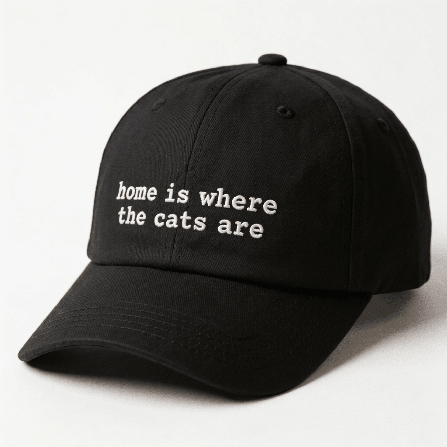 Angled front view of a black embroidered cap with home is where the cats are text on the front