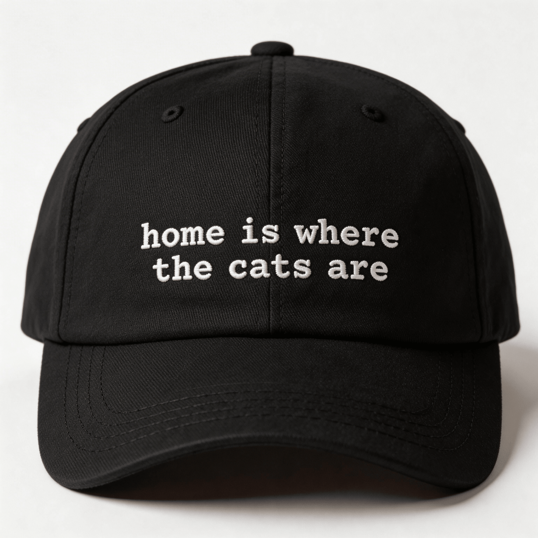Front view of a black embroidered cap with the phrase home is where the cats are in white lettering