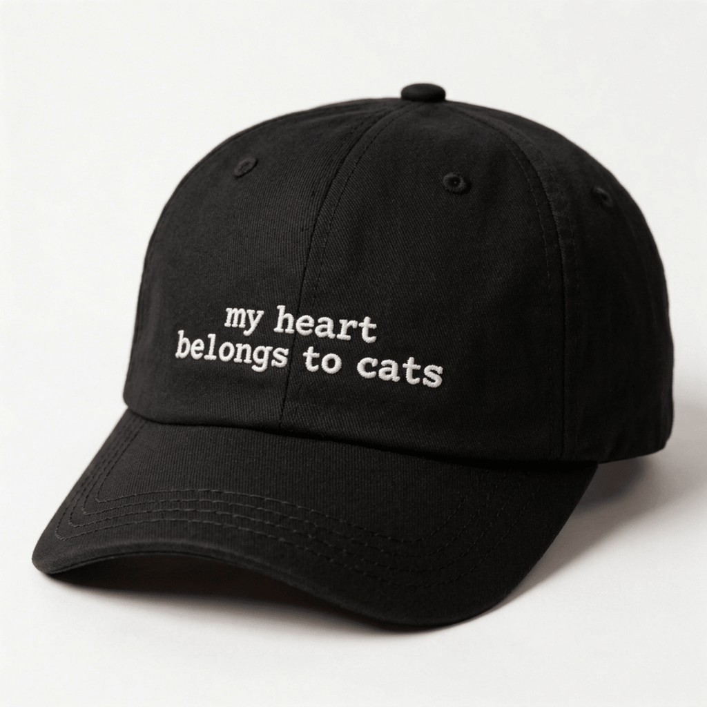 Angled front view of a black embroidered cap with my heart belongs to cats text on the front